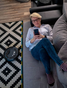 A woman relaxes on her couch while robot vacuum is cleaning