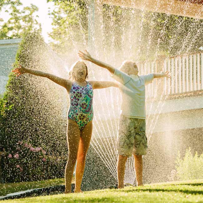 Kids outdoors playing with garden sprinkler