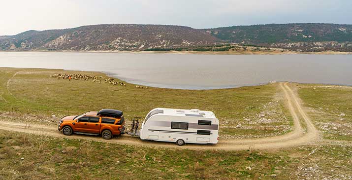 Truck pulling a camper driving along river edge